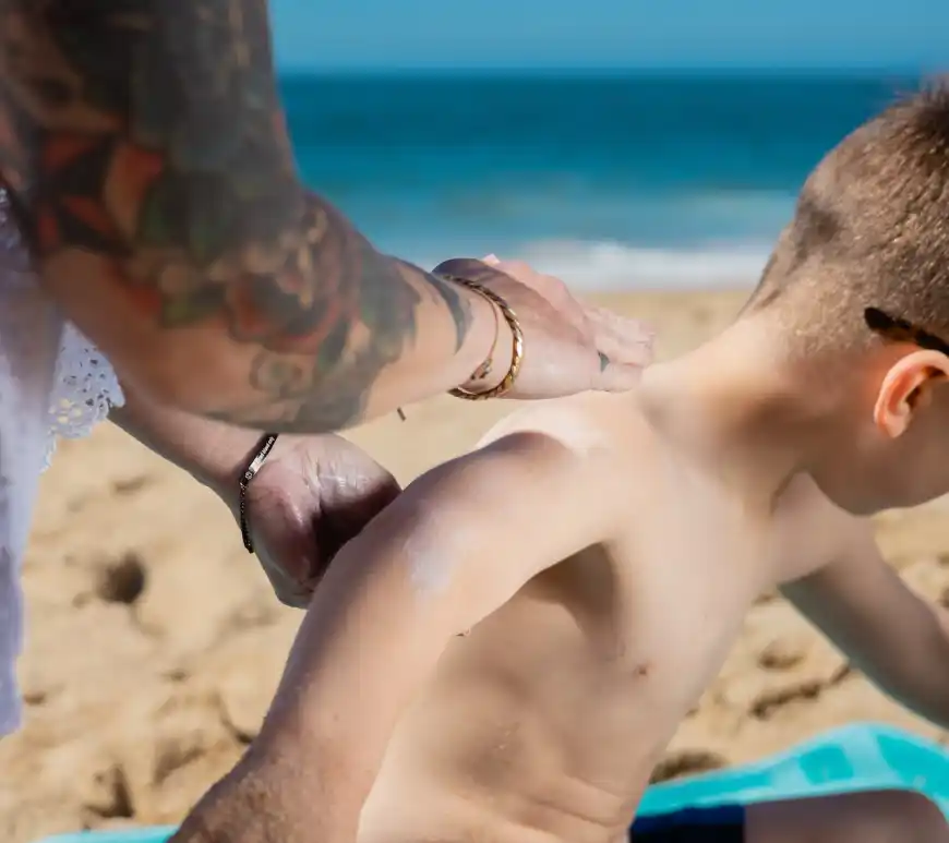 a person applying sunscreen on a boy s arm